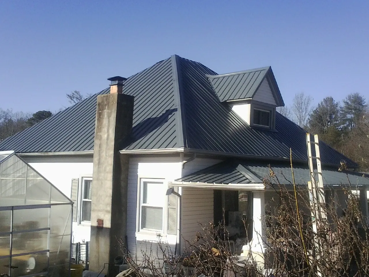 Dark blue standing seam metal roof on a white farmhouse with dormer — Slate & Tile Roof Repair by Roofing Brothers in Cornelia