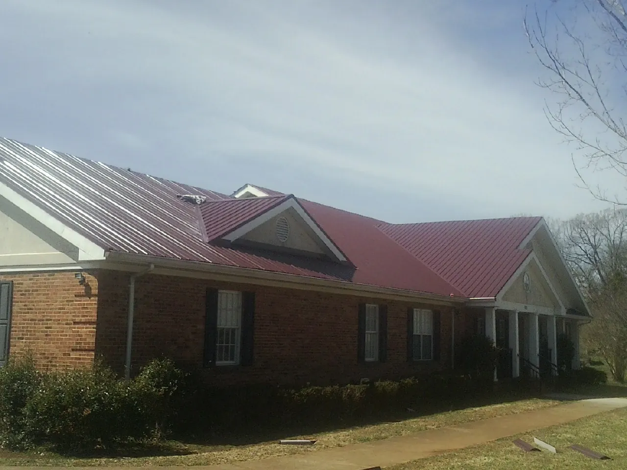 Red metal roof with gabled entries on a long brick building, from a Hail Damage Roof Repair job in Cornelia