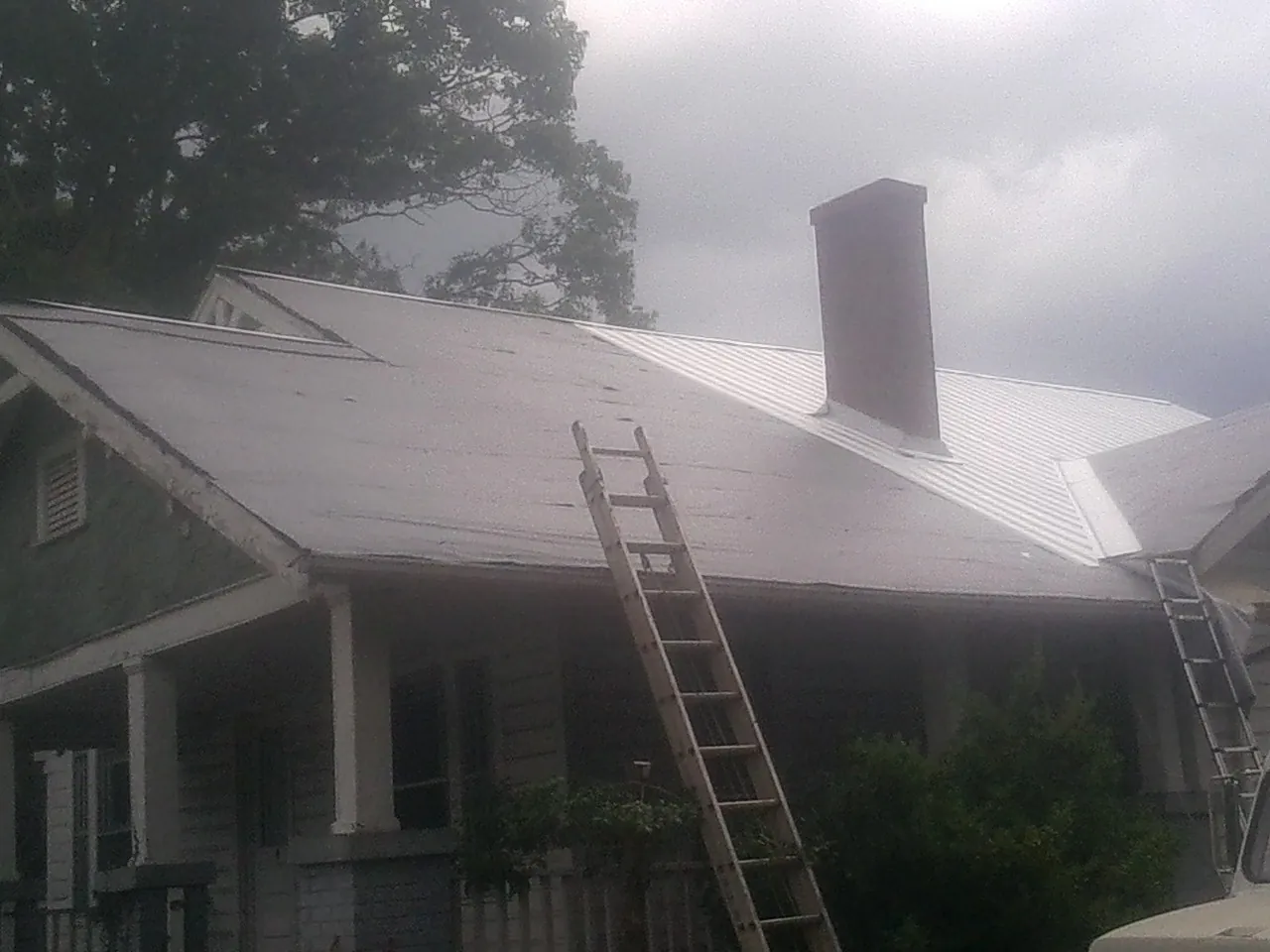 Ladders against a metal roof on an older home with a brick chimney in Cornelia