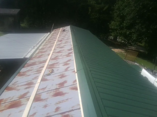Old rusted panels beside newly installed green metal roofing — Wind Damage Roof Repair by Roofing Brothers in Cornelia