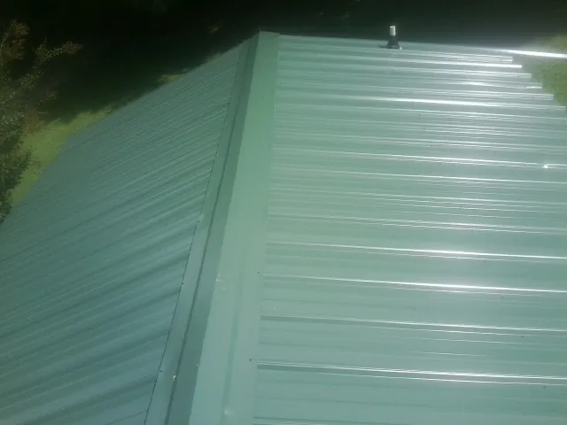 New green metal panels meeting at the ridge of a roof — Flat Roof Repair work by our crew in Cornelia
