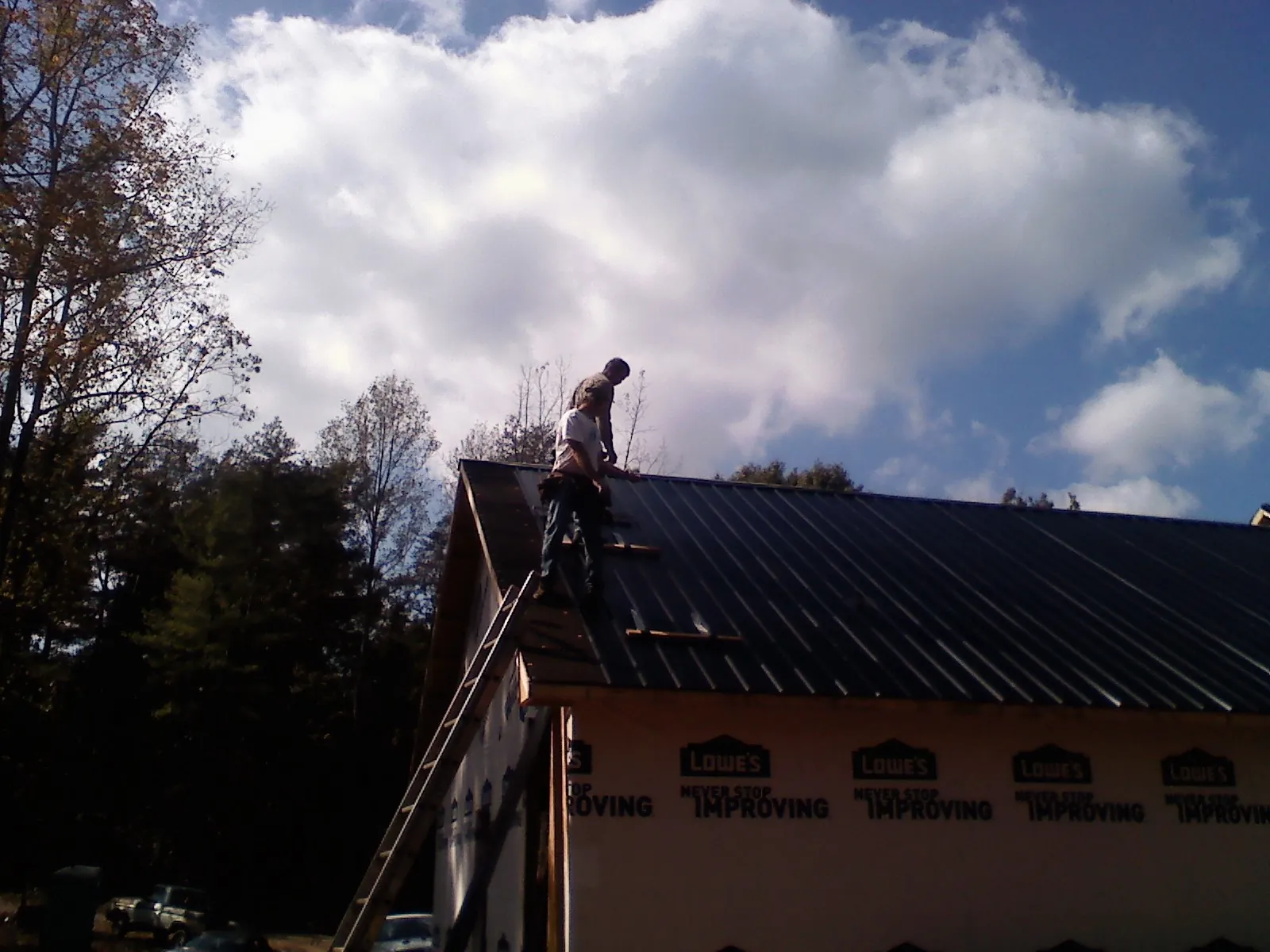 Roofer fastening dark metal panels high against a cloudy sky, from a Roof Inspection job in Cornelia