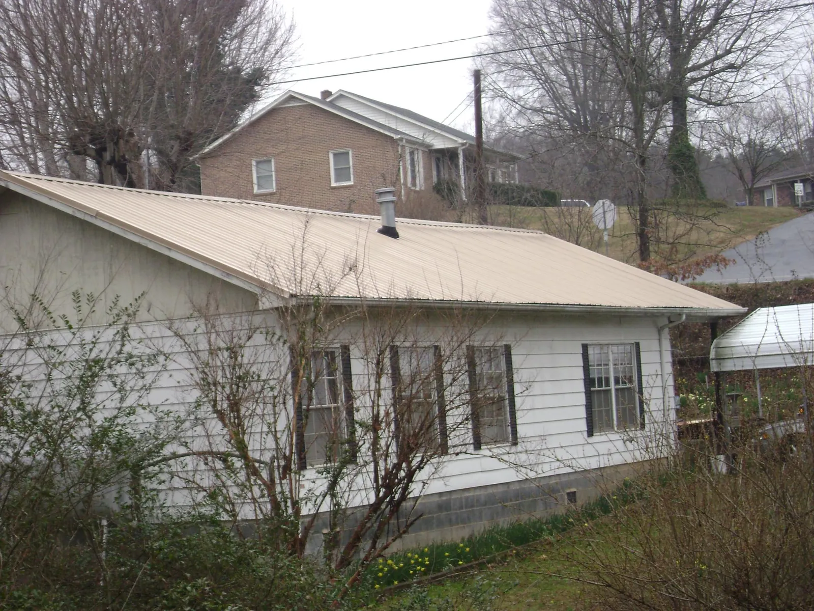 Tan metal roof on a white sided house set into a hillside — Commercial Roofing by Roofing Brothers in Cornelia
